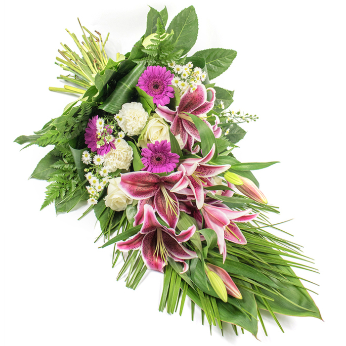 This carefully crafted funeral sheaf is photographed on a plain white background, allowing its colours and lines to stand out clearly. The arrangement runs in a gentle diagonal from top left to bottom right, creating the impression of a flowing, elongated teardrop that reflects quiet grief and loving remembrance. At its heart, large Stargazer lilies unfold, their broad petals in intense fuchsia-pink with pristine white margins and scattered burgundy spots that add depth and character. Some of the lilies are still in bud, with green casings touched by soft pink, hinting at beauty still to emerge. Surrounding these focal blooms are vivid magenta gerbera daisies, whose generous, round heads offer a warm, contemporary contrast. Creamy white roses-some tightly closed, others just beginning to open-and fluffy white carnations bring a gentle, pure quality to the design. Threaded through the arrangement, tiny white daisy-like filler flowers create a lace-like effect, softening transitions and filling spaces with delicate texture. The entire spray is embraced by a rich framework of greenery: broad, dark green leaves support the flowers from beneath; feathery fern fronds radiate outward; and long, slender, grass-like leaves sweep gracefully toward the lower right, enhancing the cascading shape. The stems are neatly gathered and bound at the top left, evidence of the careful hands at Flower Delivery Fortis Green, crafting a tribute that might be taken to a service in a local church or a quiet home near Cherry Tree Wood. Though the picture is silent, one can imagine the gently spicy lily fragrance layered with the soft scent of roses and carnations. The overall effect is one of dignified elegance and heartfelt sympathy, suited to honouring a loved one within the Fortis Green community.